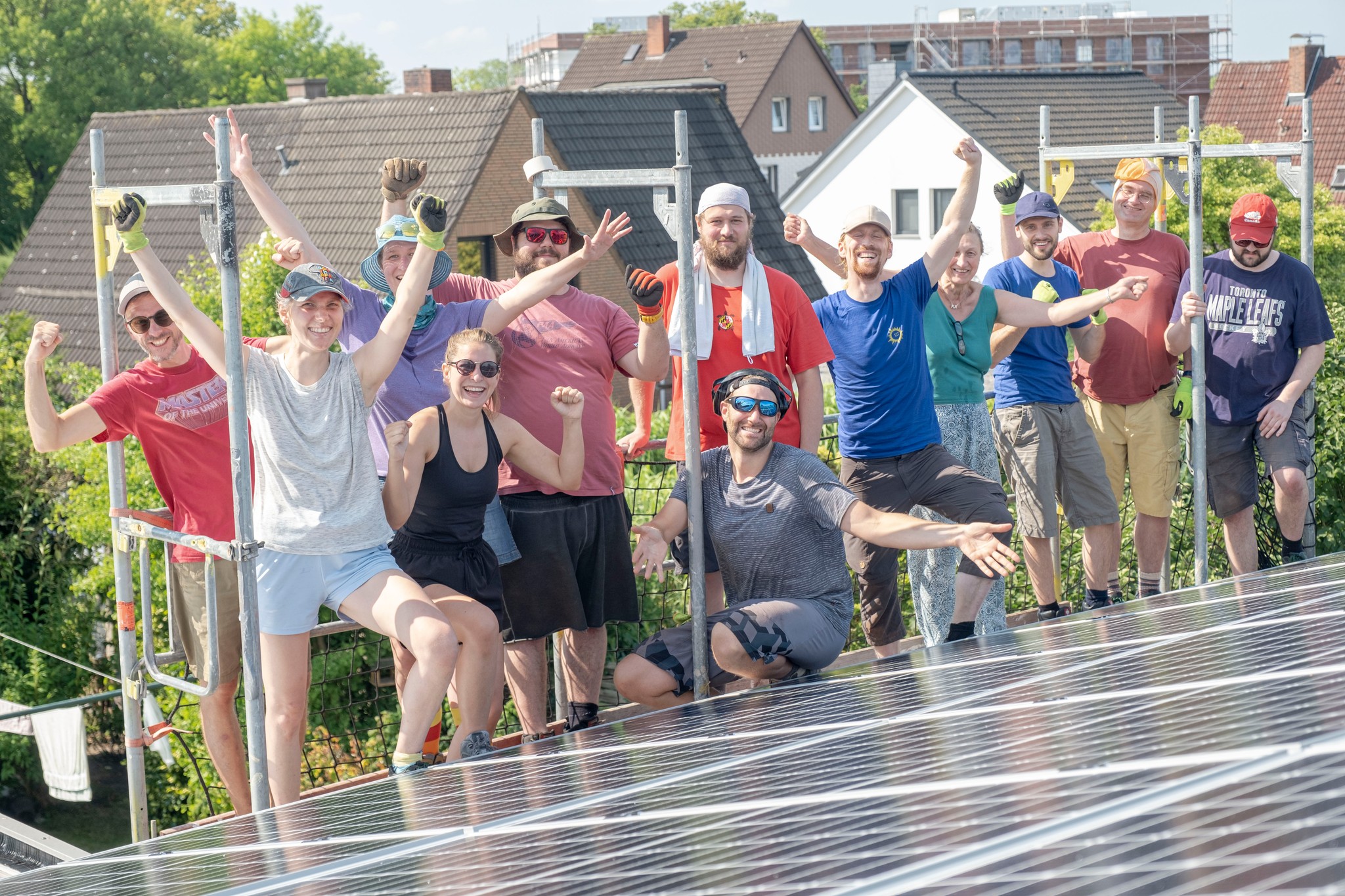 Vor dem Steildach mit einer fertig installierten Solar-Anlage stehen zehn Bauhelfer:innen und das Team vom Bremer SolidarStrom und freuen sich mit ausgestreckten Armen. Der Selbstbau-Tag war ein voller Erfolg!