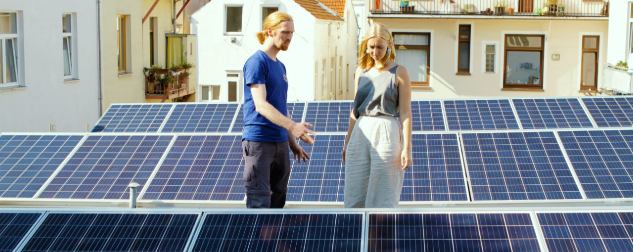 Foto von Chris und einer Kund*in auf einem sonnigen Bremer Dach mit aufgeständerten Solarmodulen. Der Bremer SolidarStrom bringt die Energiewende auf dein Dach.